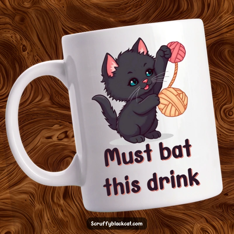 Funny kitten mug featuring a scruffy black kitten playfully batting at a dangling ball of yarn, a hilarious and cute scene.